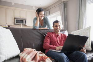 Happy man using laptop on sofa while woman looks on